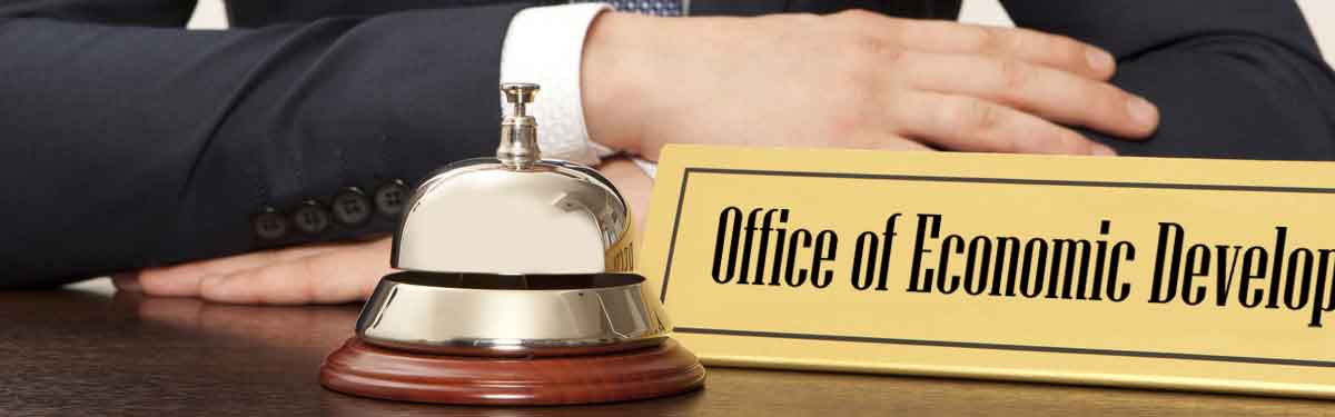 A man sits behind a desk with a bell and a brass engraved nameplate on it