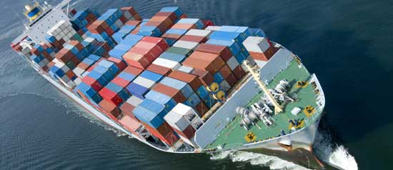 A large ship with its deck full of containers heads out to sea.