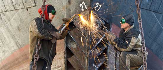 Maritime workers weld a bow plate into place