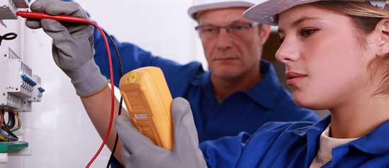 A young female technician is taught how to test electrical connections by a mentor