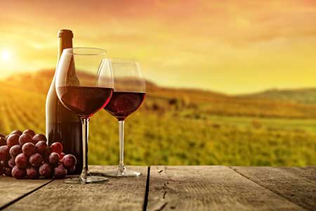 A pair of wine glasses and a bottle of wine rest on a table in a vineyard as the sun sets.