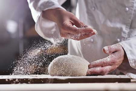 A chef flours dough being prepared for the oven.