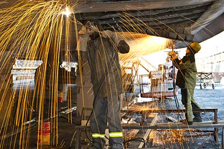 Welders work on a new boat in a shipyard, welding plates on the hull.