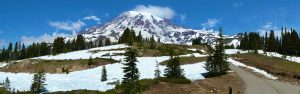 A panoramic shot of Mount Rainier with snow in the foreground.